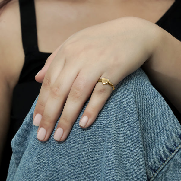 Close-up of a woman's hand wearing a yellow gold heart ring, posed on her arm for a chic look CHC Fine Jewelry