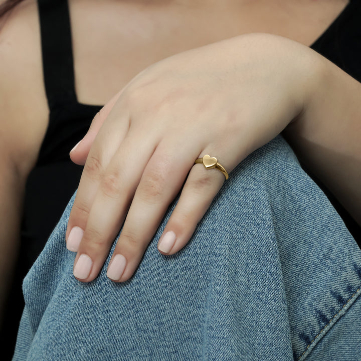 Close-up of a woman's hand wearing a yellow gold heart ring, posed on her arm for a chic look CHC Fine Jewelry